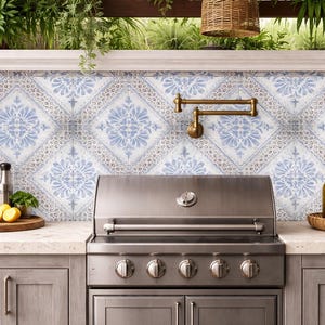 Pode incluir: Uma churrasqueira externa de a&ccedil;o inoxid&aacute;vel est&aacute; centralizada em frente a um backsplash com azulejos estampados em azul e branco. A bancada cont&eacute;m uma bandeja de madeira com lim&otilde;es, uma garrafa de azeite e outros acess&oacute;rios de cozinha.