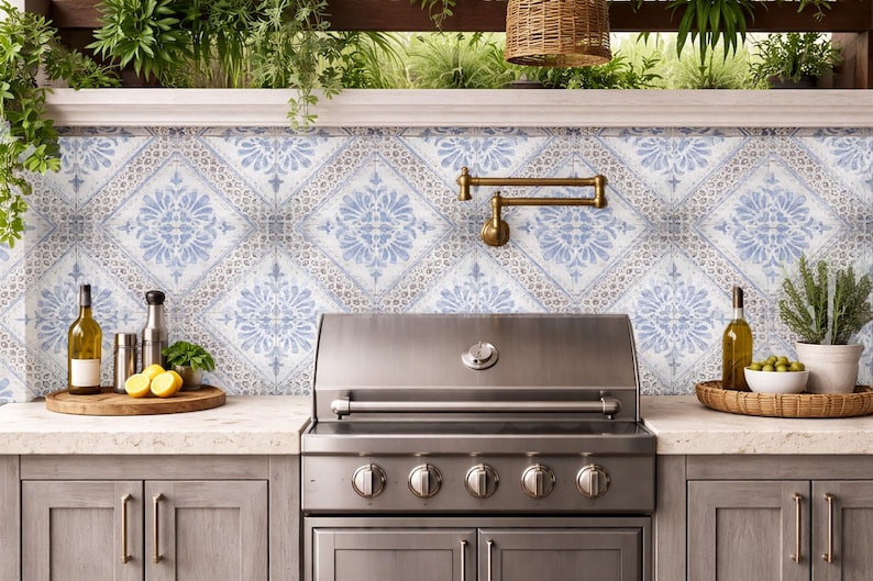 Pode incluir: Uma churrasqueira externa de a&ccedil;o inoxid&aacute;vel est&aacute; centralizada em frente a um backsplash com azulejos estampados em azul e branco. A bancada cont&eacute;m uma bandeja de madeira com lim&otilde;es, uma garrafa de azeite e outros acess&oacute;rios de cozinha.