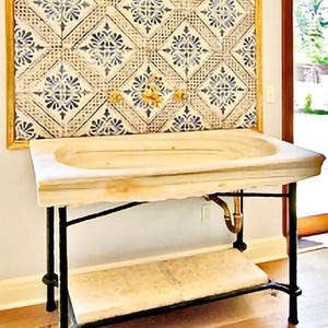 Pode incluir: Uma pia de m&aacute;rmore com uma bacia retangular fica em cima de uma estrutura de metal preto com uma prateleira inferior. A pia est&aacute; colocada contra uma parede com um painel de azulejos emoldurado com um padr&atilde;o floral azul e creme repetido. Torneiras douradas s&atilde;o vis&iacute;veis.