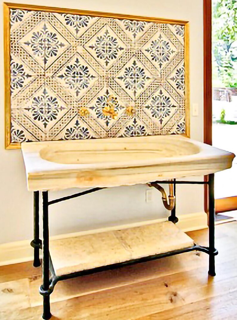 Pode incluir: Uma pia de m&aacute;rmore com uma bacia retangular fica em cima de uma estrutura de metal preto com uma prateleira inferior. A pia est&aacute; colocada contra uma parede com um painel de azulejos emoldurado com um padr&atilde;o floral azul e creme repetido. Torneiras douradas s&atilde;o vis&iacute;veis.