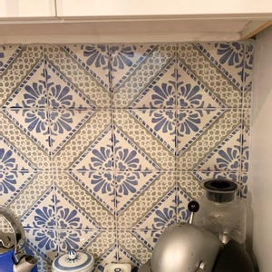 Pode incluir: Azulejos decorativos de cozinha com um padr&atilde;o floral azul e branco. Os azulejos est&atilde;o dispostos em um padr&atilde;o de losangos. Uma chaleira azul, potes e uma cafeteira s&atilde;o vis&iacute;veis na bancada.