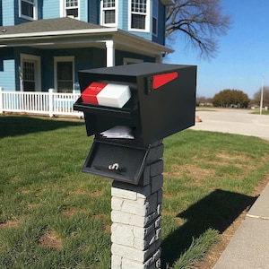 May include: A modern black mailbox with a red accent on the side, mounted on a stone pillar. The mailbox has two compartments, one open and holding mail, the other holding a stack of white and red cards.