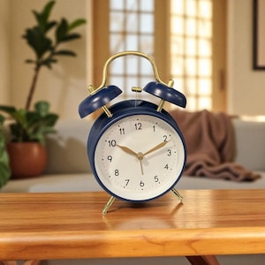 Peut inclure: Un réveil bleu marine avec un cadran blanc et des accents dorés. La montre a un design classique avec deux cloches sur le dessus et des pieds dorés. Le cadran affiche l'heure avec des chiffres noirs et des aiguilles dorées.