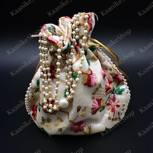 May include: A white drawstring bag with floral embroidery and a pearl beaded chain. The bag is made of satin and has a gold drawstring.