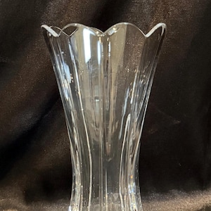 Può includere: Vaso di vetro trasparente con bordo smerlato e design svasato e a coste. Il vaso ha una base ampia e si assottiglia verso l'alto, creando una forma visivamente accattivante. Il vetro riflette la luce. Ideale per i fiori.
