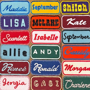 Op de afbeelding: Een verzameling van 15 kleurrijke stoffen patches met daarop gestikte namen. De patches zijn rechthoekig en hebben een witte achtergrond met kleurrijke stiksels rond de randen. De namen op de patches zijn Maddie, September, Shiloh, Lisa, McLane, Kate, Scarlett, Isabelle, September, Allie, Andy, Cassidy, Renee, Ronald, Morgan, Georgia, Gabi en Charlene.