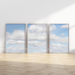 May include: Three framed prints of a blue sky with white clouds. The prints are arranged in a row on a white wall.
