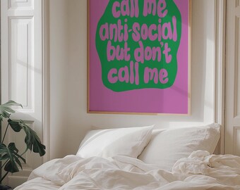 May include: A framed poster with the text "call me anti-social but don't call me" in green on a pink background. The poster is hanging above a bed with white bedding. Books are stacked on the bed.