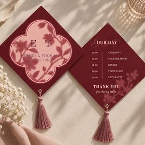 以下が含まれることがあります： ダスティローズのタッセルが付いた、ひし形のバーガンディ色の結婚式招待状2枚。左側のカードには、イニシャルE T、名前Esmée & Thomas、日付01.06.2029が記された四つ葉のフレームがあります。右側のカードにはOur Dayのスケジュールが記載されています。