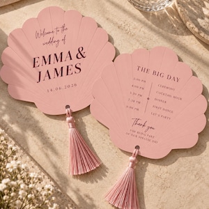 Puede incluir: Dos abanicos de papel en forma de concha de color rosa empolvado con texto oscuro. Uno dice Welcome to the wedding of EMMA & JAMES 14.06.2026. El otro detalla el horario THE BIG DAY de 15:00 a 21:00 y Thank you for being part of our special day.