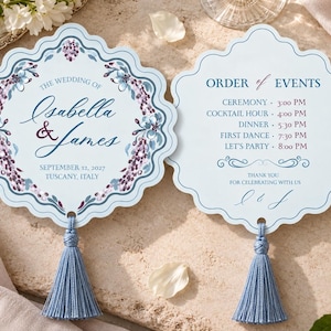 May include: Two scalloped-edge wedding cards in light blue with a floral border. One card reads The Wedding of Isabella & James, September 12, 2027, Tuscany, Italy. The other reads Order of Events with a schedule from 3:00 PM to 8:00 PM.