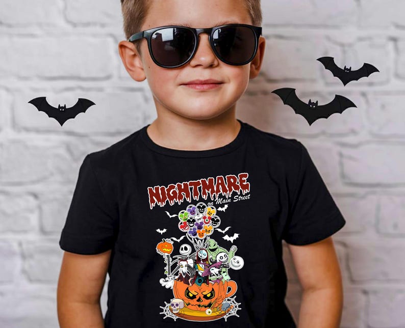 May include: A black t-shirt featuring a Halloween-themed graphic. The design includes characters from "The Nightmare Before Christmas" inside a jack-o'-lantern, with the text "Nightmare on Main Street". The shirt is worn by a person wearing sunglasses.