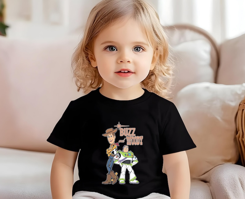 Puede incluir: Una camiseta negra con un gr&aacute;fico de Buzz Lightyear y Woody de Toy Story. El texto "Buzz Woody" est&aacute; impreso en marr&oacute;n en la camiseta.