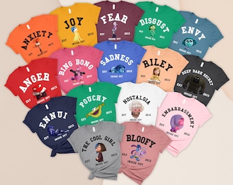Puede incluir: Una colección de camisetas coloridas con personajes y palabras de la película "Del revés". Cada camiseta muestra una emoción diferente, como "Alegría", "Tristeza" y "Ira", con ilustraciones y el año "2015".