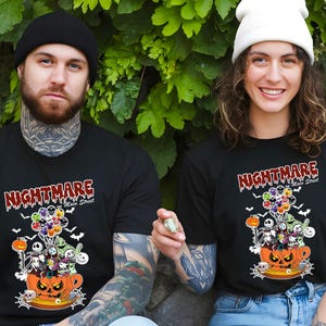 May include: Black t-shirts with a Halloween-themed graphic. The design features the text "Nightmare on Main Street" above a pumpkin-shaped teacup filled with cartoon characters and balloons. Bats and other spooky elements complete the design.
