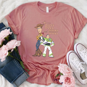 Puede incluir: Una camiseta rosa con un gr&aacute;fico de Buzz Lightyear y Woody de Toy Story. El texto "Buzz and Woody" est&aacute; impreso en la camiseta.