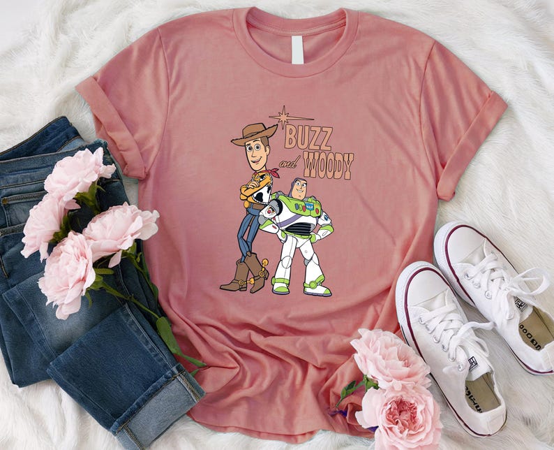 Puede incluir: Una camiseta rosa con un gr&aacute;fico de Buzz Lightyear y Woody de Toy Story. El texto "Buzz and Woody" est&aacute; impreso en la camiseta.