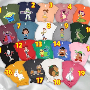 Può includere: Una collezione di diciannove magliette colorate con vari personaggi del film d'animazione Toy Story. Le magliette sono in vari colori, tra cui verde, blu, arancione, rosa e nero, ognuna con una grafica unica del personaggio.