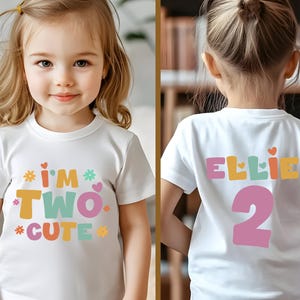 May include: White t-shirt with the text "I'M TWO CUTE" in colorful letters and graphics. The back of the shirt says "ELLIE" and the number "2". The shirt is designed for a two-year-old.