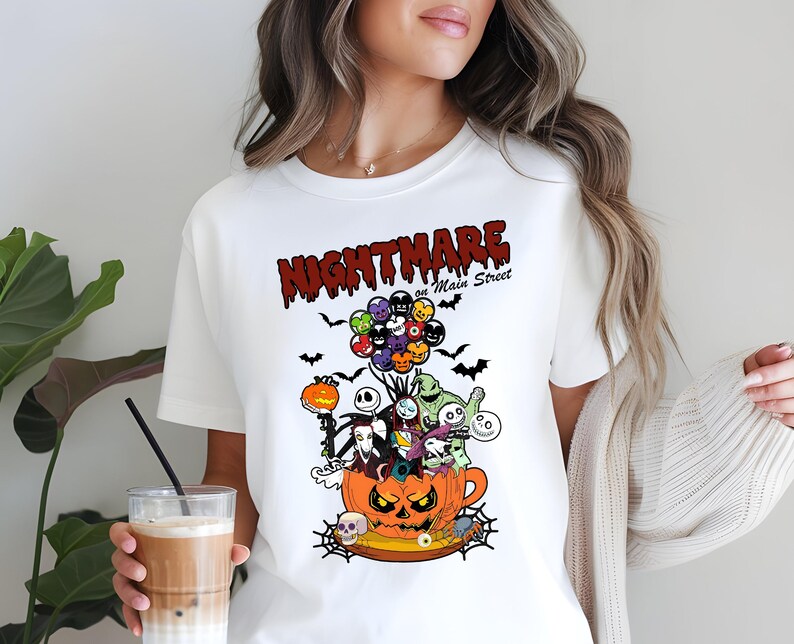 May include: White t-shirt featuring a colorful graphic design with the text "NIGHTMARE on Main Street." The design includes characters from The Nightmare Before Christmas, a pumpkin, bats, and balloons.