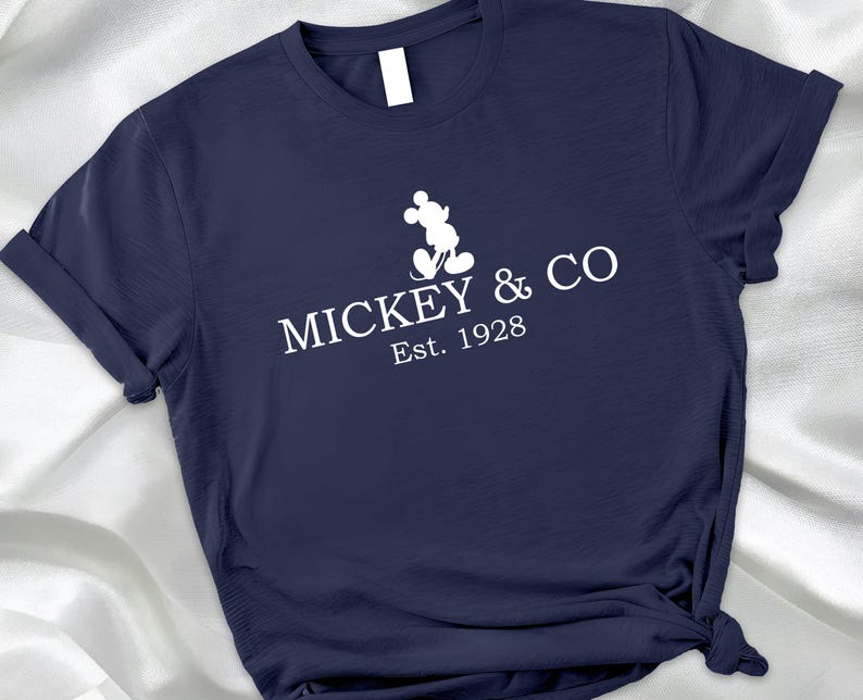 May include: Navy blue t-shirt featuring a white Mickey Mouse silhouette and the text "MICKEY & CO Est. 1928". The shirt is made of a soft material and has a classic crew neck design.