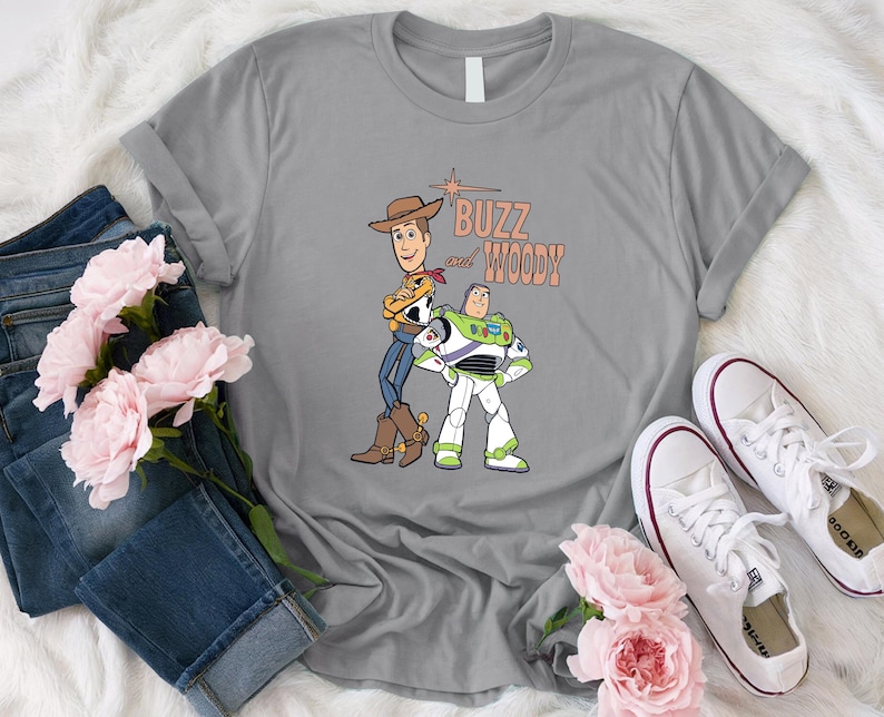 Puede incluir: Camiseta gris con un gr&aacute;fico de Buzz Lightyear y Woody de Toy Story. El texto "Buzz and Woody" est&aacute; impreso en naranja en la camiseta.