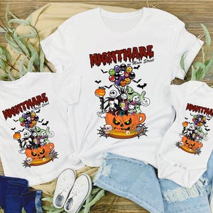 May include: White t-shirts and a onesie featuring a Halloween-themed graphic. The design includes a jack-o'-lantern, characters, and the text "Nightmare on Main Street". The graphic is in orange, black, and other colors.