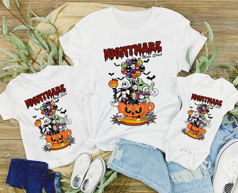May include: White t-shirts and a onesie featuring a Halloween-themed graphic. The design includes a jack-o'-lantern, characters, and the text "Nightmare on Main Street". The graphic is in orange, black, and other colors.