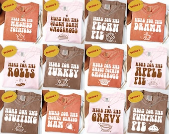 May include: A collection of twelve t-shirts in various colors, each featuring the phrase "Here for the" followed by a Thanksgiving food item. The shirts have a retro font and include images of the food items.