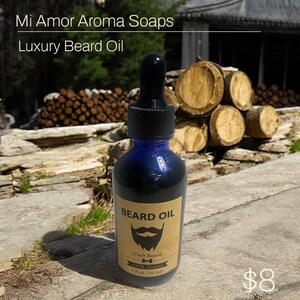 May include: A blue glass bottle of beard oil with a black dropper. The label reads "BEARD OIL" with a beard illustration and "Craft Beard 100% Natural 1 fl oz (30 ml)". The text "Mi Amor Aroma Soaps Luxury Beard Oil" is at the top.