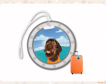 May include: A round luggage tag featuring a porthole design with a silver frame and a white plastic loop. The center displays an illustration of a brown dog with a shaggy coat wearing an orange vest against a blue sky and sea background.