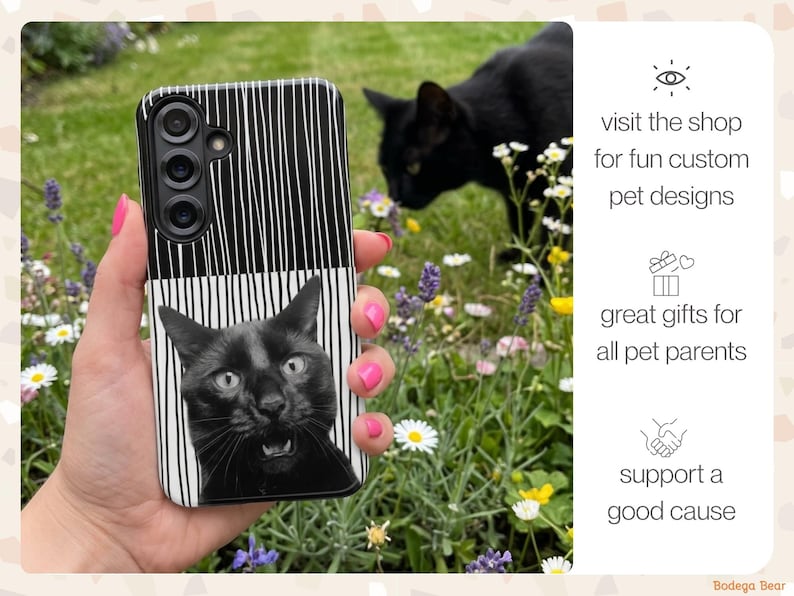 A custom Tough Case for a Galaxy S25 with a portrait of a funny black cat looking surprised against a black and white striped background. The phone is being held up in front of a garden where the real black cat is smelling the flowers. The captions read: visit the shop for more custom pet designs, great gift for all pet parents, and support a good cause.