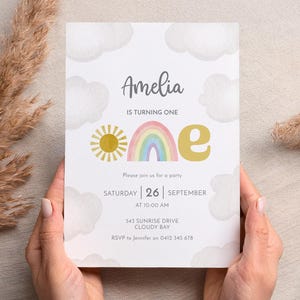 May include: A birthday invitation with the name "Amelia" at the top. The invitation features a watercolor design with a sun, rainbow, and clouds. The text reads "IS TURNING ONE" and includes party details: date, time, and location.