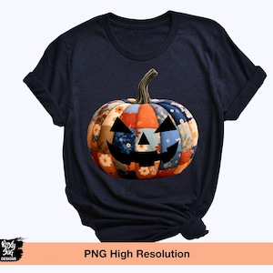 Puede incluir: Camiseta azul marino con un diseño de calabaza de retazos y una cara tallada. La calabaza está hecha de varias telas florales y estampadas en colores naranja, azul y crema. La camiseta tiene mangas enrolladas.