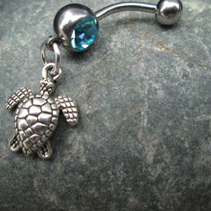 May include: A silver belly button ring with a blue gem and a silver turtle charm.