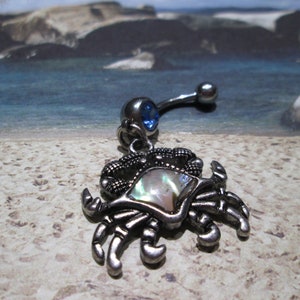 May include: A silver belly button ring with a blue gem and a charm of a silver crab with a mother-of-pearl shell.
