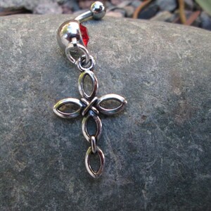 May include: Silver body piercing with a red gem and a dangling cross charm.