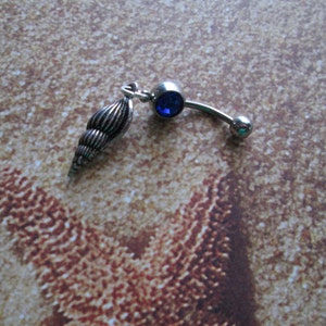 May include: Silver belly button ring with a blue gem and a silver seashell charm.