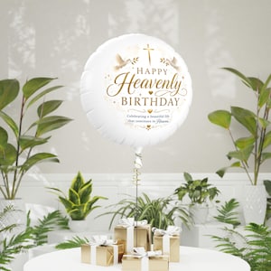 May include: A round white foil balloon featuring gold text that reads Happy Heavenly Birthday and Celebrating a beautiful life that continues in Heaven, accented with gold doves, a cross, and small stars, tied to gold gift boxes.