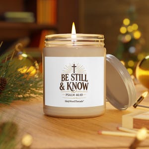 Peut inclure: Une bougie beige allumée dans un bocal en verre avec une étiquette blanche. L'étiquette porte l'inscription "BE STILL & KNOW" avec une croix et l'écriture "PSALM 46:10". La bougie est ouverte, avec le couvercle à côté.