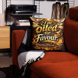 May include: Square decorative pillow with the text "I'm Oiled for Favour" in gold lettering. The pillow features doves, books, and a pouring vessel design on a black background. The brand name "HolyWordThreads" is at the bottom.