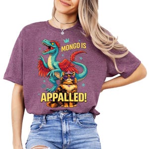 May include: A purple t-shirt with a cartoon dinosaur in teal and red, and a cat wearing sunglasses and a crown. The text "MONGO IS APPALLED!" is printed in yellow.