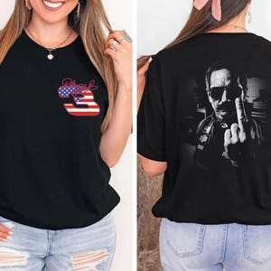 以下が含まれることがあります： アメリカ国旗柄で塗りつぶされた数字の3と署名が前面にプリントされた黒の半袖Tシャツ。背面には、サングラスをかけた男性のモノクロ写真がプリントされています。