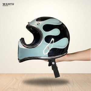 Peut inclure: Casque de moto avec un motif de flammes bleu clair et noir. Le casque est orné d'une bordure argentée et d'une jugulaire noire. La marque "WAHYU" est visible en haut à gauche.