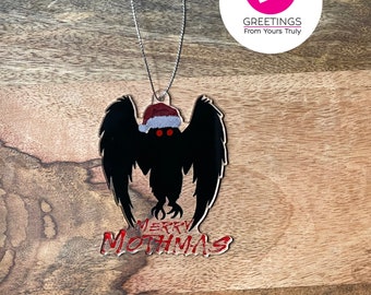 May include: A black mothman ornament with red eyes and a Santa hat. The ornament says "Merry Mothmas" in red lettering.