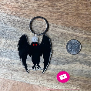 Peut inclure: Un porte-cl&eacute;s en acrylique noir et rouge repr&eacute;sentant la silhouette d'une cr&eacute;ature aux grandes ailes et aux yeux rouges brillants. Le porte-cl&eacute;s est attach&eacute; &agrave; un anneau en m&eacute;tal argent&eacute;.