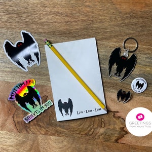 Peut inclure: Un ensemble de produits d&eacute;riv&eacute;s sur le th&egrave;me de Mothman comprenant un autocollant, un porte-cl&eacute;s, un bouton et un bloc-notes. L'autocollant est holographique et pr&eacute;sente un motif arc-en-ciel. Le porte-cl&eacute;s et le bouton sont noirs et pr&eacute;sentent une silhouette de Mothman avec des yeux rouges. Le bloc-notes est blanc et porte l'inscription "Live - Love - Lurk".