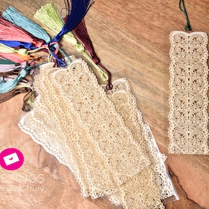 May include: A collection of cream-colored lace bookmarks with colorful tassel accents. The bookmarks feature intricate floral patterns and are displayed on a wooden surface. The image also includes the text "GREETINGS From Yours Truly".