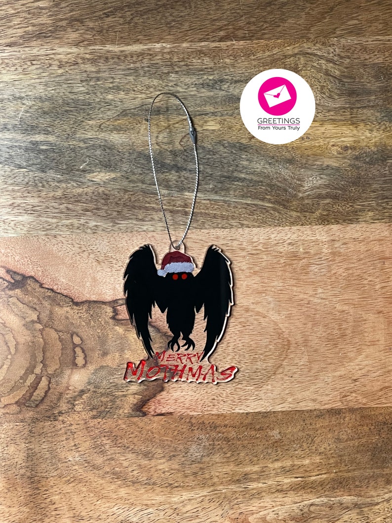 May include: A black and red Christmas ornament featuring a mothman with a Santa hat and the text "Merry Mothmas".