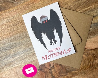 May include: A white card with a black silhouette of a mothman wearing a Santa hat. The text "Merry Mothmas" is written in red below the mothman.